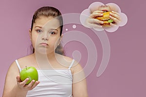 The girl eats a green Apple, but dreams about hamburger. Harmonious and healthy food for children. Child eating healthy snack.