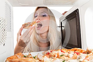 Girl eats pizza out of the microwave
