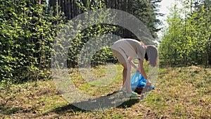 A girl eco activist collects garbage in the forest, in the summer. A volunteer collects plastic bottles in the park, in nature.