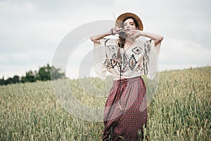Girl in eco style clothes posing in nature background. Portrait of young woman in boho hat. Pretty ethno stranger in field