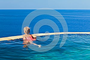 Girl at edge of infinity swimming pool with sea view