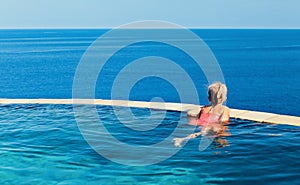 Girl at edge of infinity swimming pool with sea view