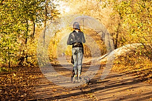 A girl on an electric scooter in the fall under a transparent umbrella rides through the autumn forest along the road, walks in
