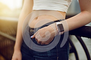 Girl with electronic watch holding hand at jeans pocket in city at sunset time.