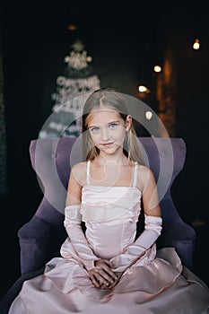 Girl in elegant dress sitting in a chair on the background of Christmas decorations