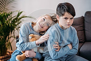 Girl embracing offended boy sitting on sofa at home