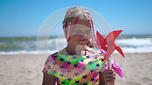 Girl on an empty sandy beach with a red toy windmill