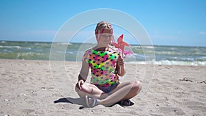 Girl on an empty sandy beach with a red toy windmill