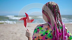 Girl on an empty sandy beach with a red toy windmill