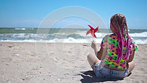 Girl on an empty sandy beach with a red toy windmill