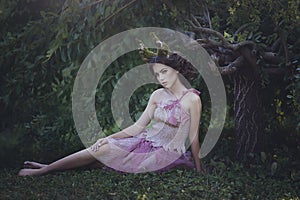 Girl enchanted Princess with horns sitting under a tree. Girl Mystical creature fawn in shabby clothes in a fairy forest