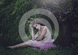 Girl enchanted Princess with horns sitting under a tree. Girl Mystical creature fawn in shabby clothes in a fairy forest