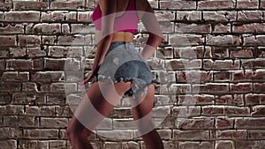 Girl energetic in the crop top and denim shorts dance twerk against a brick wall. Slow motion. Close up
