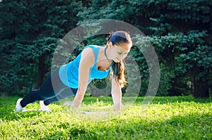 Girl is engaged in fitness in the park, doing exercises. Training on the street in the summer morning. Concept sport healthy