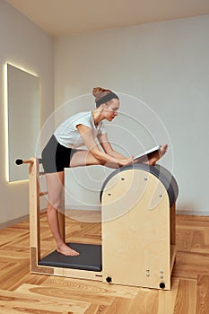 A girl is engaged in Pilates on the reformer reading a book, Pilates classes on the reformer, strengthening the