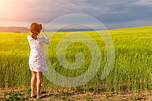 Girl enjoying green wheat field in countryside. Field of wheat blowing in the wind at sunny spring day. Young and green Spikelets