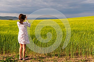 Girl enjoying green wheat field in countryside. Field of wheat blowing in the wind at sunny spring day. Young and green Spikelets