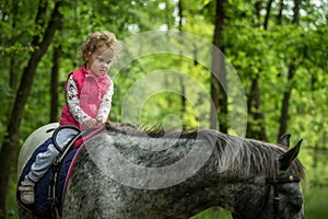 Girl enjoying horseback riding in the woods, young pretty girl with blond curly hair on a horse with backlit leaves