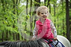 Girl enjoying horseback riding in the woods, young pretty girl with blond curly hair on a horse with backlit leaves