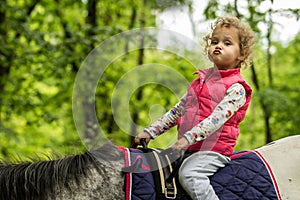 Girl enjoying horseback riding in the woods, young pretty girl with blond curly hair on a horse with backlit leaves