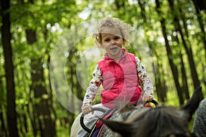 Girl enjoying horseback riding in the woods, young pretty girl with blond curly hair on a horse with backlit leaves