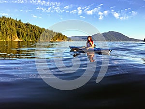 A girl enjoying kayaking on the beautiful and calm ocean waters of Howe Sound, off of Gambier Island, British Columbia, Canada.