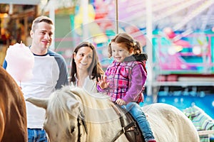 Girl enjoying pony ride, fun fair, parents watching her