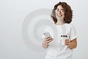 Girl enjoying spending time laughing over new memes. Portrait of beautiful creative curly-haired woman in trendy glasses