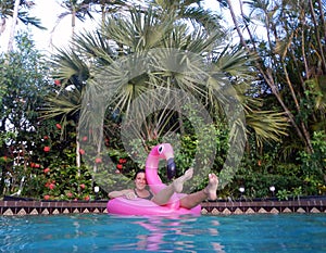 Girl enjoying in the swimming pool on flamingo float