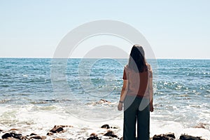 The girl is enjoying the view of the sea. The sea, the rocks, the wave and the sun.