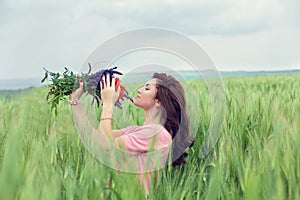 Girl enjoying in a wheat-field perfume of a bouquet of flowers