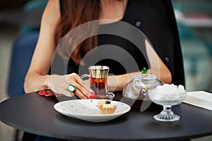 Girl enjoys cup of Turkish tea alone in cozy cafe. Hands close up with glass and teapot on black table