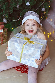 The girl enthusiastically holds gift sitting near the Christmas tree