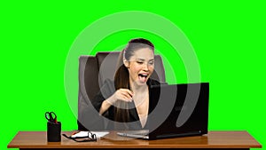 Girl enthusiastically works behind a laptop, smiles and enjoys the result. Green screen