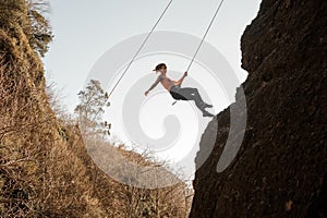 Girl equipped with a rope abseiling on the sloping rock