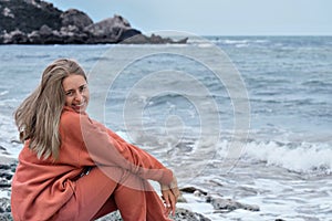 A girl of European appearance with long brown hair sits on the seashore and enjoys a moment and a beautiful look, prays
