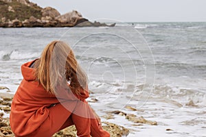 A girl of European appearance with long brown hair sits on the seashore and enjoys a moment and a beautiful look, prays