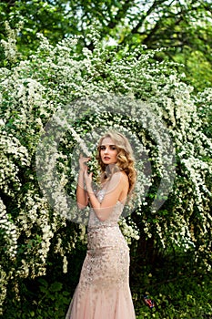 Girl in evening cocktail dress on a spring in the middle among flowering bushes and trees beautiful smiling