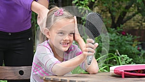 Girl examines himself in mirror while combing her mom