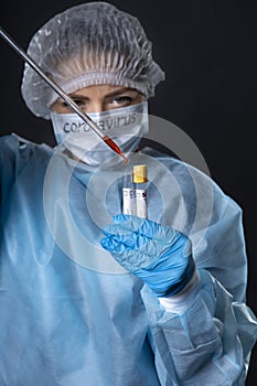 Girl examines a test tube with biomaterial. Young woman in protective clothing. On the face of a protective medical mask