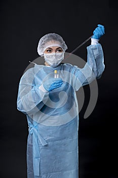 Girl examines a test tube with biomaterial. Young woman in protective clothing. On the face of a protective medical mask. A drop