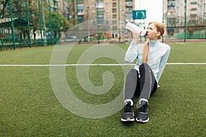 Girl after exercise, drinking water on the football field. Portrait of beautiful girl in sportswear.