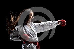 Girl exercising karate punch and screaming against black background