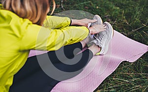 Girl exercising outdoors in sun summer day, fitness woman in trainer stretching exercises legs training outside on green park