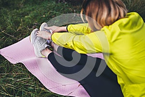 Girl exercising outdoors on yoga mat, fitness woman sneaker stretching exercises legs training outside on green grass. Sportswoman