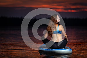 Girl exercising yoga on paddleboard in the sunset on scenic lake Velke Darko