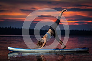 Girl exercising yoga on paddleboard in the sunset on scenic lake Velke Darko