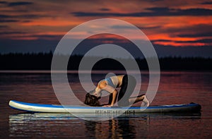 Girl exercising yoga on paddleboard in the sunset on scenic lake Velke Darko