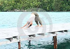 Girl exercising yoga pose downward-facing dog on jetty by sea