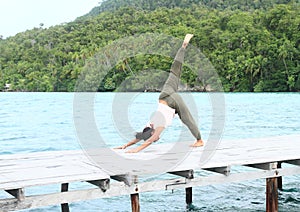 Girl exercising yoga pose three-legged downward dog on jetty by sea